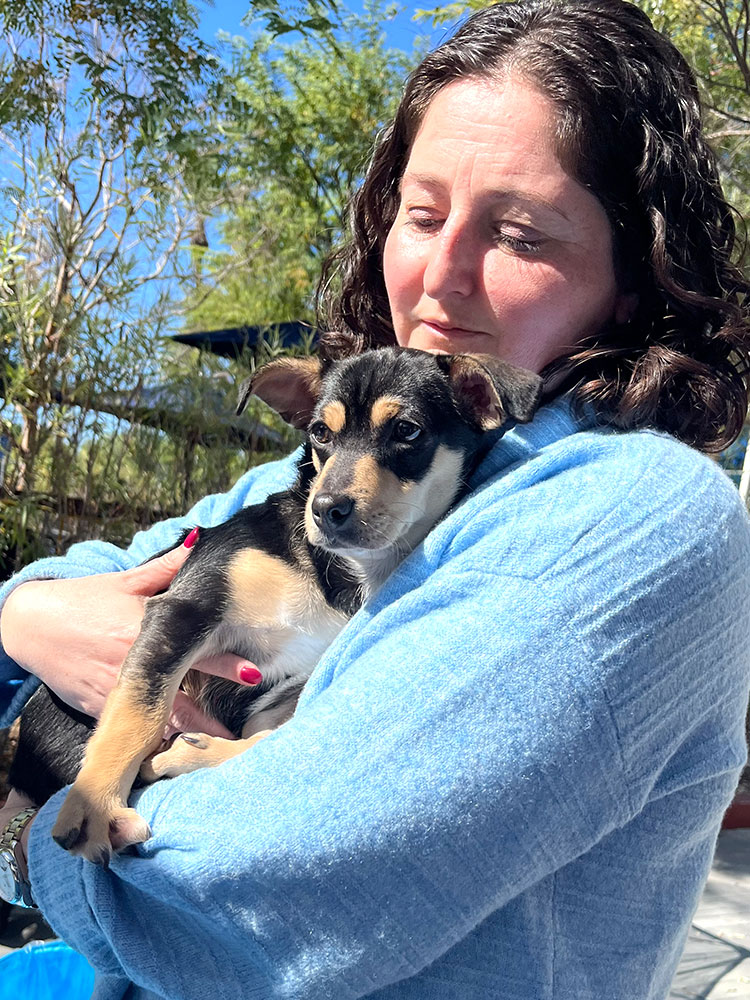 A woman in a blue shirt holding a puppy and smiling - feeling the benefits of adding Puppy Love to their Las Vegas company wellness programs.
